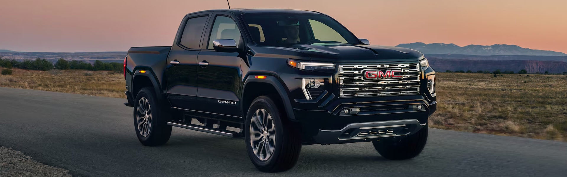 Black 2026 GMC Canyon pickup truck driving on a desert highway