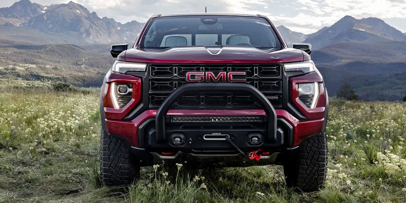 Front view of a red 2026 GMC Canyon parked in a grassy mountain landscape