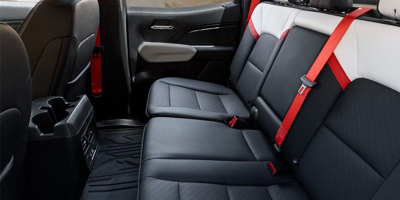 Rear passenger interior seating of the 2026 GMC Canyon with black leather seats and red seat belts