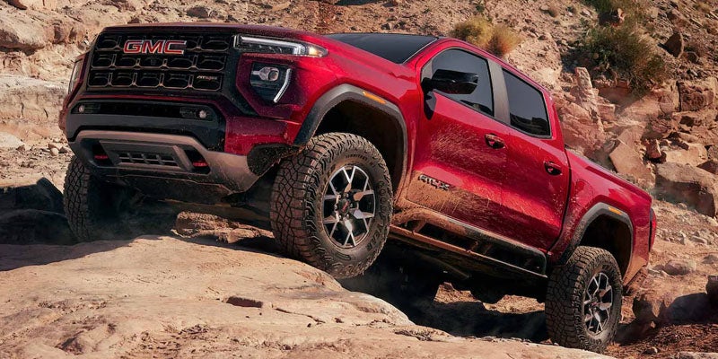 Red 2026 GMC Canyon AT4X off-road pickup truck climbing over rocky desert terrain